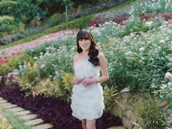 Miss Summer Summer standing among flowering garden beds in a white ruffled dress