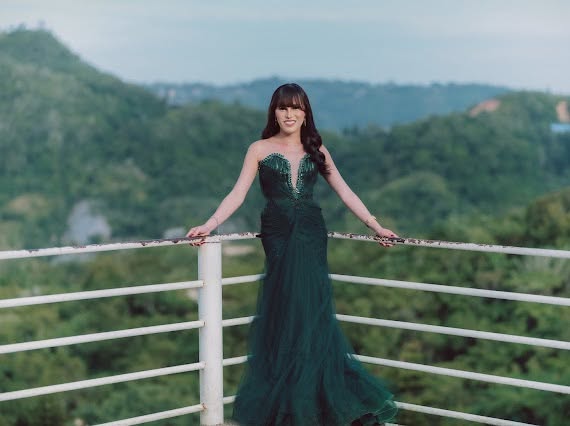 Miss Summer Summer in an emerald beaded gown at a white railing overlooking the mountains