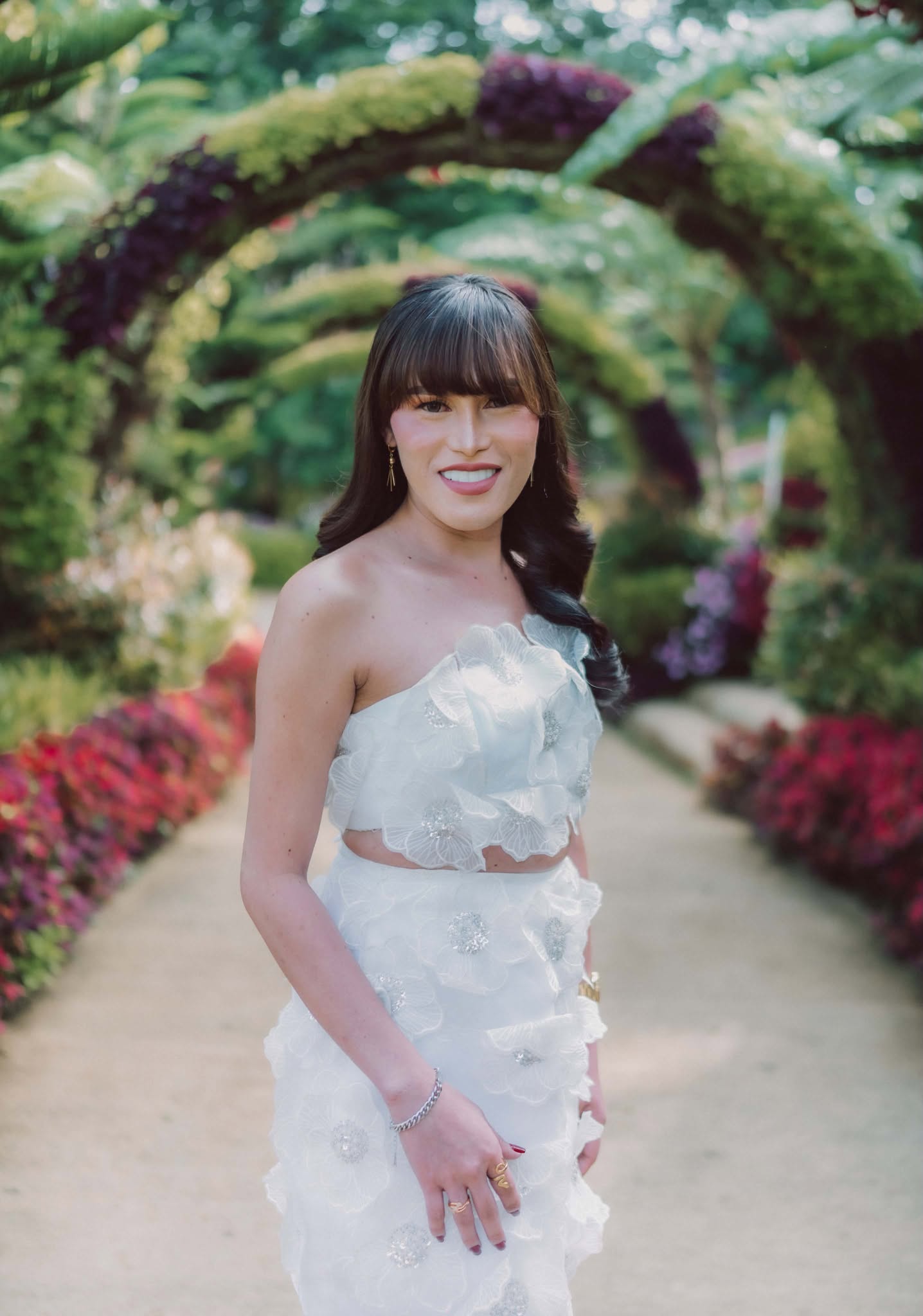 Miss Summer Summer in a white floral gown beneath a flowering garden archway