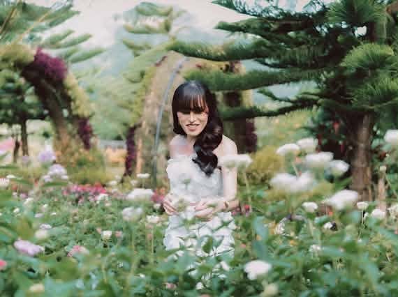 Miss Summer Summer in a white off-shoulder dress among white roses beneath tall pines