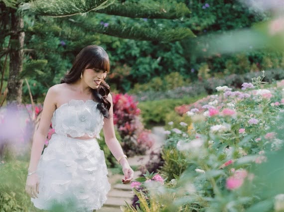Miss Summer Summer in a white floral dress walking a rose-lined garden path